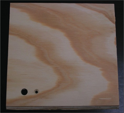 The top of the base has been cut and the front edge has been beveled to a 45° angel. Holes have been drilled for the momentary contact switch (large) and red LED (small).